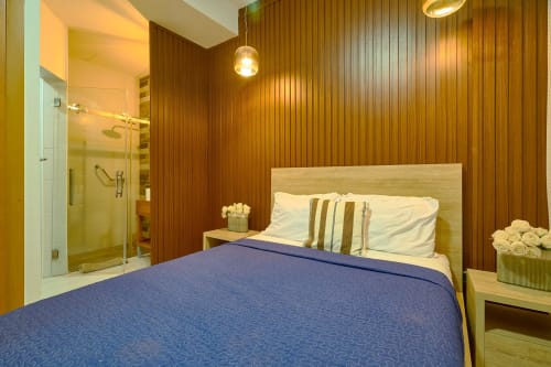 Luxurious bedroom with wood-paneled walls, blue bedding, wooden headboard, ensuite bathroom with glass shower at Booking RD