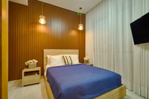 Modern bedroom with blue bedding, wood accent wall, pendant lighting, and flat-screen TV at luxury apartment in Santo Domingo