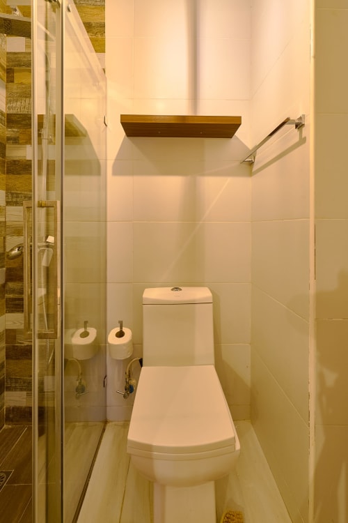 Modern bathroom in luxury downtown Santo Domingo apartment with white toilet, wooden shelf, and glass shower enclosure