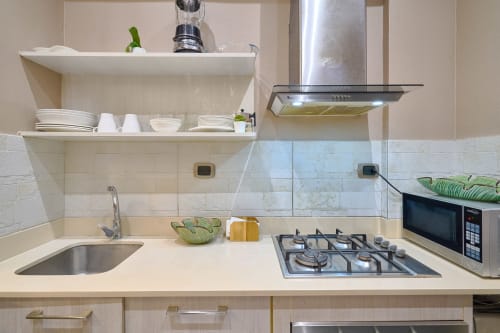 Modern apartment kitchen in Santo Domingo with gas cooktop, stainless steel hood, sink, and white tile backsplash