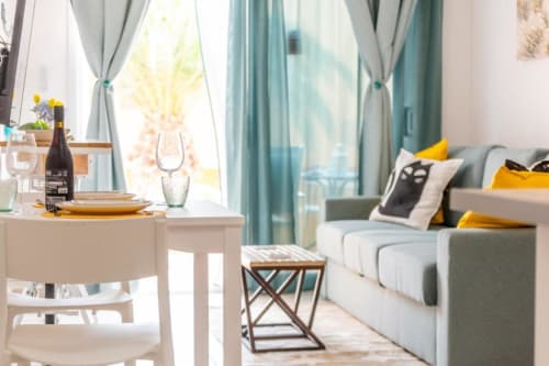 Moderno estudio en Smart Rent Fuerteventura con zona de comedor, sofá, cortinas turquesas y detalles luminosos