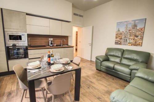 Moderno appartamento open-plan a Le Due Piazze Genova con cucina, tavolo da pranzo, divano in pelle verde e opere d'arte con veduta cittadina