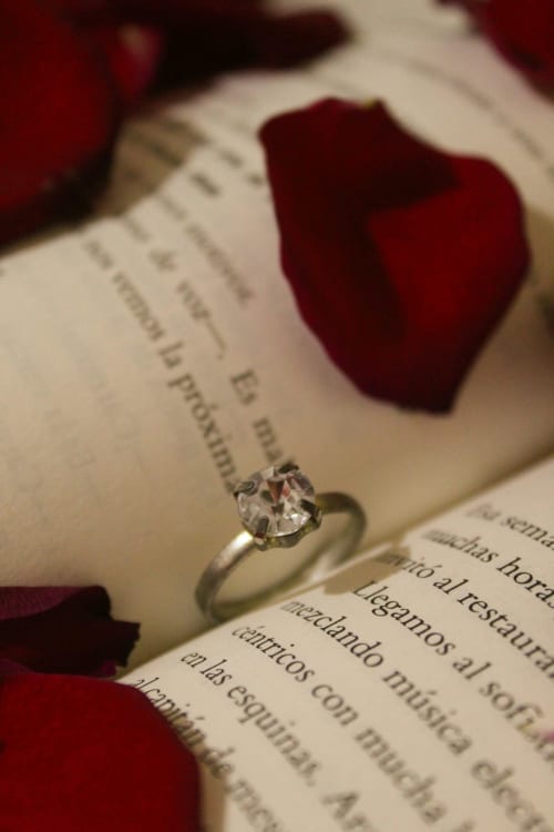 Anello di fidanzamento con diamante su libro aperto con petali di rosa rossa presso l'Agritusmo Stecadò, Dolceacqua