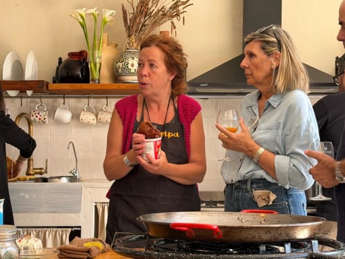 Dos mujeres en la clase de cocina de Cala Pipa en Tarragona, preparando paella en una gran sartén en la cocina moderna