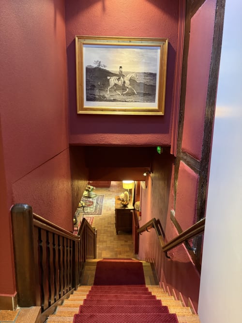 Grand escalier de l'Hôtel de l'Ange à Niedermorschwihr aux murs rose-rouge, rampes bois et décor équestre classique