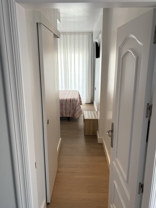 Pasillo del Hostal Juan Carlos en Carboneras que conduce a una habitación doble con colcha de rayas rojas y puertas blancas