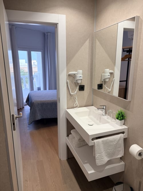 Baño moderno en el Hostal Juan Carlos de Carboneras con lavabo blanco, espejo y vista hacia el dormitorio