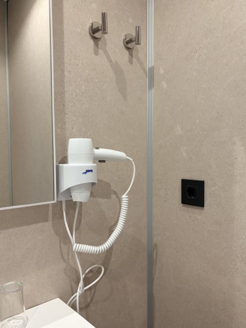 Pared del baño del Hostal Juan Carlos en Carboneras con grifería mural, secador de pelo blanco y elementos eléctricos negros