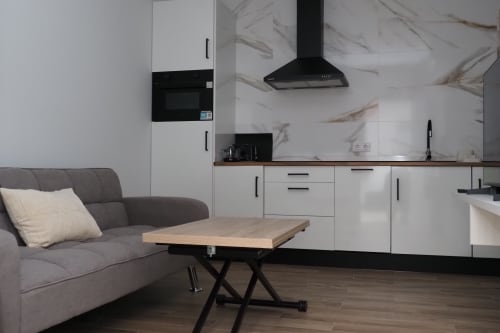 Moderna cocina y sala de estar en hostal El Camionero con backsplash de mármol, muebles blancos y sofá gris