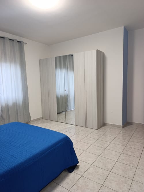 Camera da letto spaziosa con letto blu, armadio con specchi e pavimenti piastrellati nell'appartamento Tales of Abruzzo ad Atessa, Italia