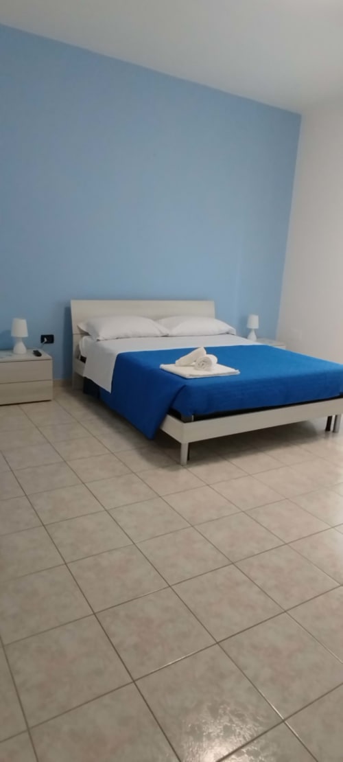Camera moderna all'hotel Tales of Abruzzo di Atessa con parete blu chiaro, letto bianco, coperta blu e piastrelle