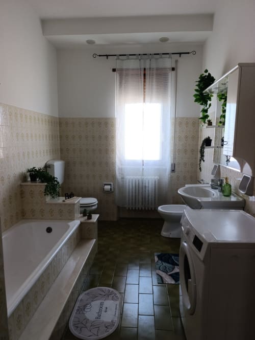 Bagno luminoso con piastrelle beige decorate, sanitari bianchi, vasca, doppio lavabo e piante in vaso in DUE ORIZZONTI