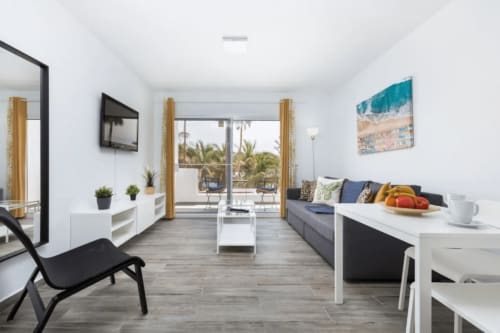 Moderna sala de estar en Smart Rent Fuerteventura con vistas al océano, sofá, comedor y arte playero
