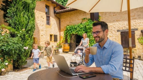 Homme travaillant sur son ordinateur portable dans la cour du gîte Le Clos Des Anges à Bagnols, en famille