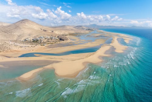 Vista aérea de las playas vírgenes de Fuerteventura con dunas de arena dorada, aguas turquesas y montañas costeras