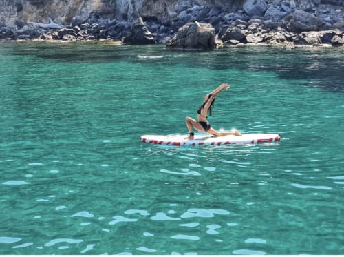 Donna che pratica paddleboard nelle acque turchesi del Mediterraneo vicino alle scogliere rocciose di Casale Artemisia, Capalbio, Toscana