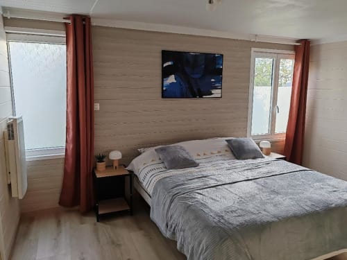 Chambre moderne aux Gites De Petrocoriis à Boulazac avec lit, TV, rideaux rouges et lambris bois