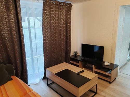 Salon moderne du gîte Les Gites De Petrocoriis avec mobilier en bois, téléviseur écran plat et rideaux marron à motifs