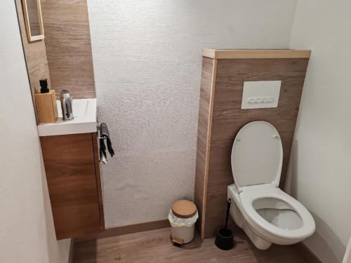 Salle de bain moderne du gîte Les Gites De Petrocoriis avec toilettes blanches, meuble vasque, lambris bois et cabine de douche