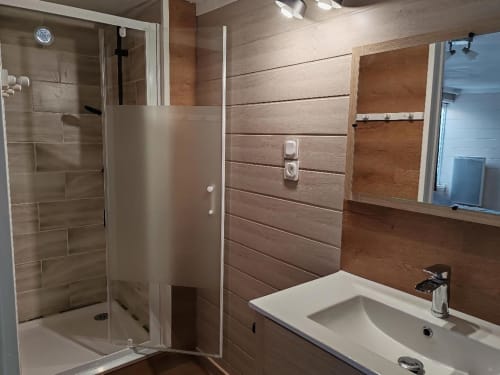 Salle de bain moderne aux Gites De Petrocoriis avec murs lambrisés, douche vitrée et lavabo blanc.
