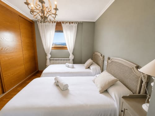 Dormitorio luminoso en dúplex Lar de Mar de Holibai en Baiona con dos camas, armario de madera, vistas al mar y araña