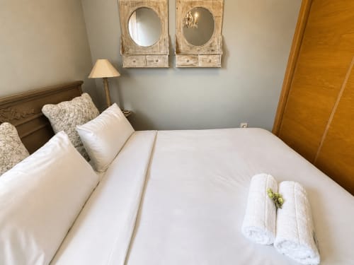 Luminoso dormitorio en Holibai Baiona con ropa de cama blanca, toallas enrolladas, espejos y lámpara en apartamento moderno
