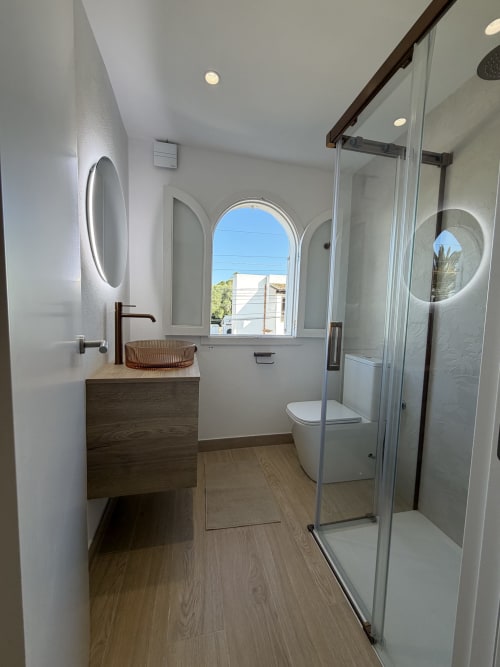 Modern bathroom at Villa Alegria in Cala d'Or with vessel sink, walk-in shower, and arched window.