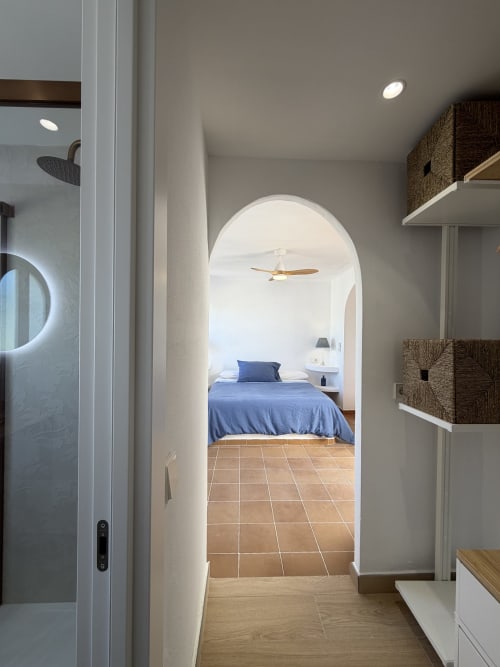Bathroom entrance to bedroom at Villa Alegria, Cala d'Or. Archway view of blue bed and ceiling fan.