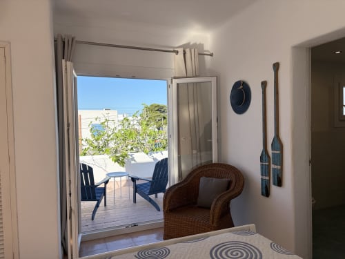 Dormitorio luminoso en Villa Alegria Cala d'Or con puertas abiertas a terraza, silla de mimbre y decoración acuática