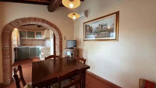Sala da pranzo di lusso con tavolo in legno, cucina con volta in mattoni, TV e arte urbana incorniciata a Borgo di Erboli