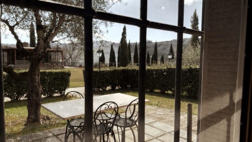 Patios del Borgo di Erboli con arredamento in metallo, cipressi e vista sulle colline toscane dell'appartamento a Cavriglia