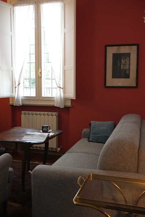 Elegant red living room at Cristallo Apartment in Ravenna with gray sofa, wooden desk, and French doors