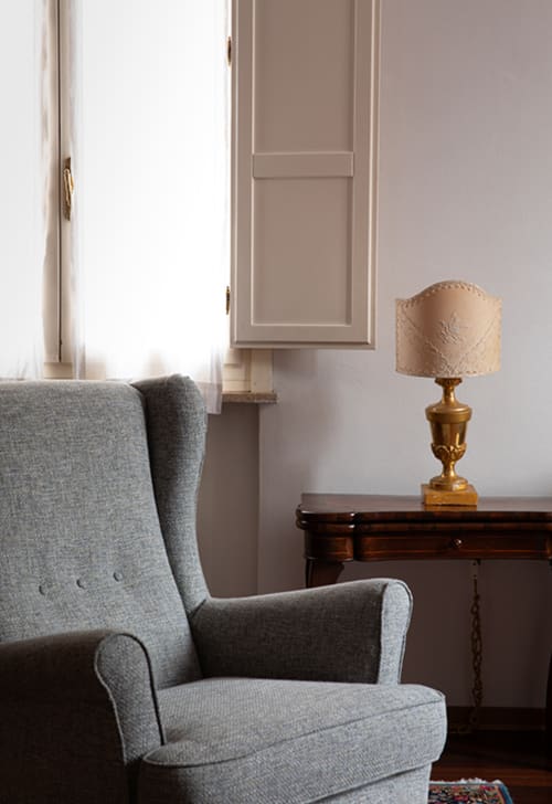 Gray wingback chair with lamp and desk in Cristallo Apartment, Ravenna