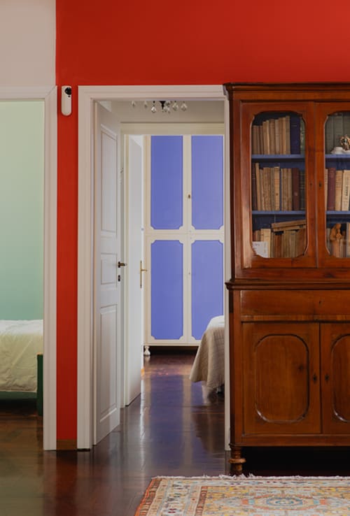 Cristallo Apartment in Ravenna: modern interior with red accent wall, blue doors, wooden cabinet, and parquet flooring