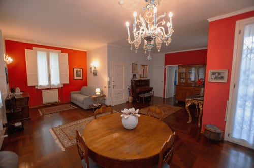 Elegant dining room at Cristallo Apartment in Ravenna with red walls, wooden table, chandelier, and classic furnishings