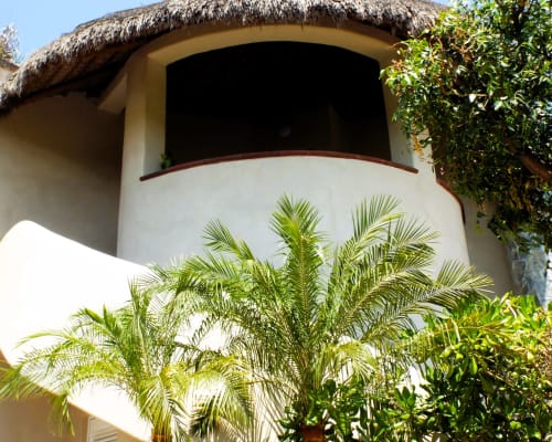 Edificio blanco curvo con techo de paja en El Origen Villas & Spa, Puerto Escondido, rodeado de plantas tropicales