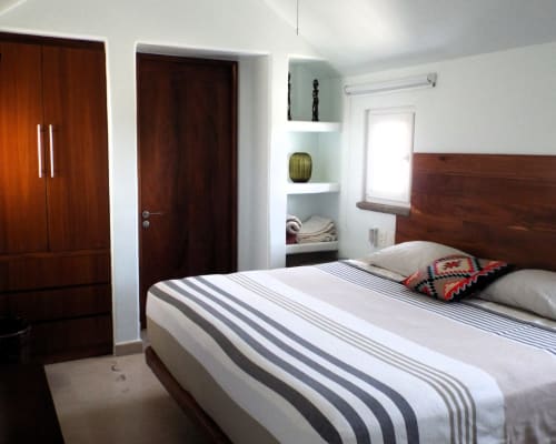 Dormitorio moderno en El Origen Villas & Spa, Puerto Escondido con cama de rayas, muebles de madera y vista al océano