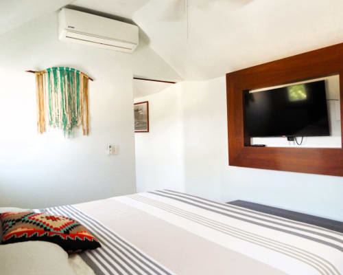 Habitación moderna en El Origen Villas & Spa, Puerto Escondido, con TV pantalla plana, ropa de cama a rayas y acceso a vista al océano.