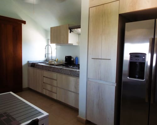 Cocina moderna en apartamento de Puerto Escondido con gabinetes de madera clara, electrodomésticos de acero inoxidable y encimeras grises