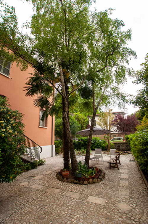 Cristallo Apartment courtyard in Ravenna with mature trees, seating area, and terracotta building facade