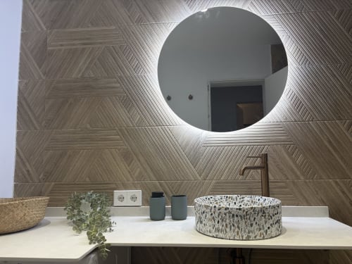 Modern bathroom at Villa Alegria with illuminated circular mirror, herringbone wood tiles, and speckled stone sink in Cala