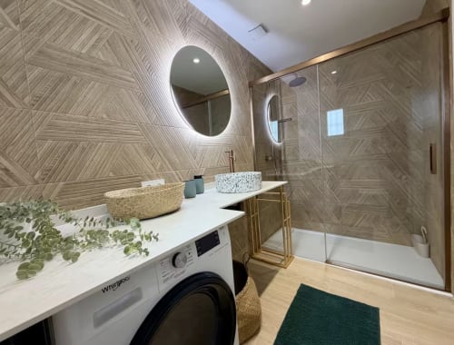 Modern bathroom at Villa Alegria Cala d'Or with illuminated mirror, geometric tile walls, vessel sink, and walk-in shower