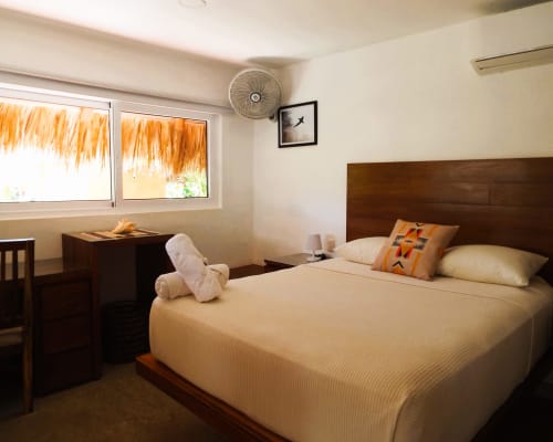 Habitación espaciosa en El Origen Villas con cama de madera oscura, ropa de cama crema y vistas al jardín a través de amplios ventanales en Puerto