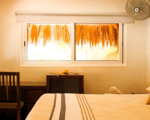 Habitación luminosa con ropa de cama a rayas, ventanas con techo de mimbre con vista al jardín de Puerto Escondido, ventilador de techo