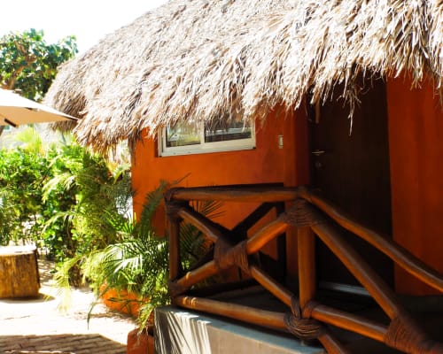 Bungalow naranja con techo de palapa y terraza de madera en El Origen Villas & Spa, Puerto Escondido
