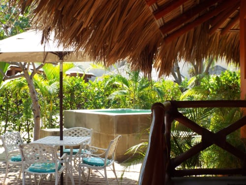 Terraza privada en El Origen Villas con muebles de patio blancos, techo de palapa y vistas a exuberante jardín tropical
