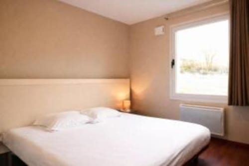 Chambre lumineuse avec lit blanc, murs crème et grande fenêtre donnant sur Picherande à l'hôtel-appartements Les Balcons du Sancy
