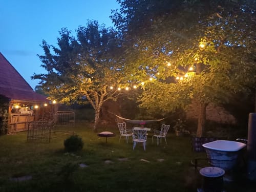 Gezellige buitenruimte bij L'escale du Banquet met slingers, zitplaatsen en vuurkorf onder bomen in Mhère