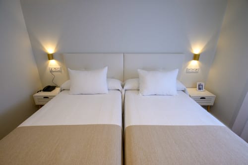 Camas gemelas en habitación moderna y luminosa del Hotel Boutique Alcazaba Salobreña con apliques de pared y ropa de cama blanca