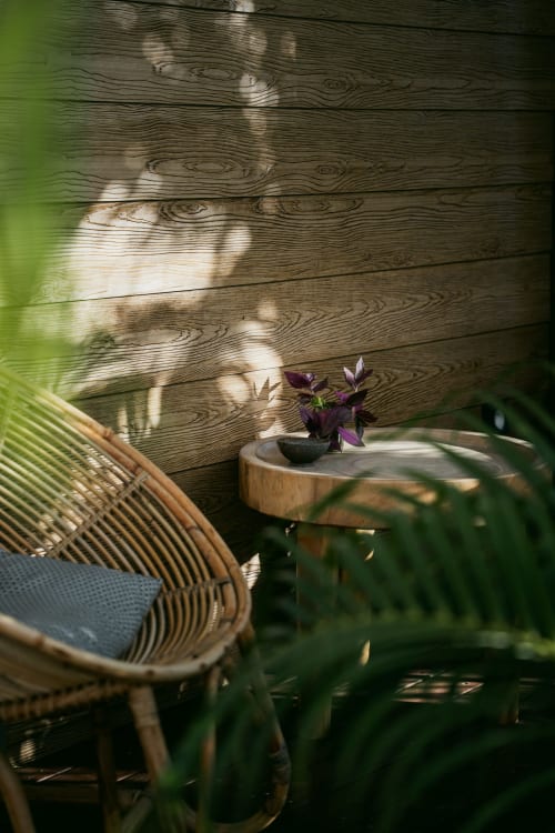 Chaise en rotin sur terrasse en bois avec fleurs violettes et vue sur le jardin du gîte Ô Coeur de l'Ouest